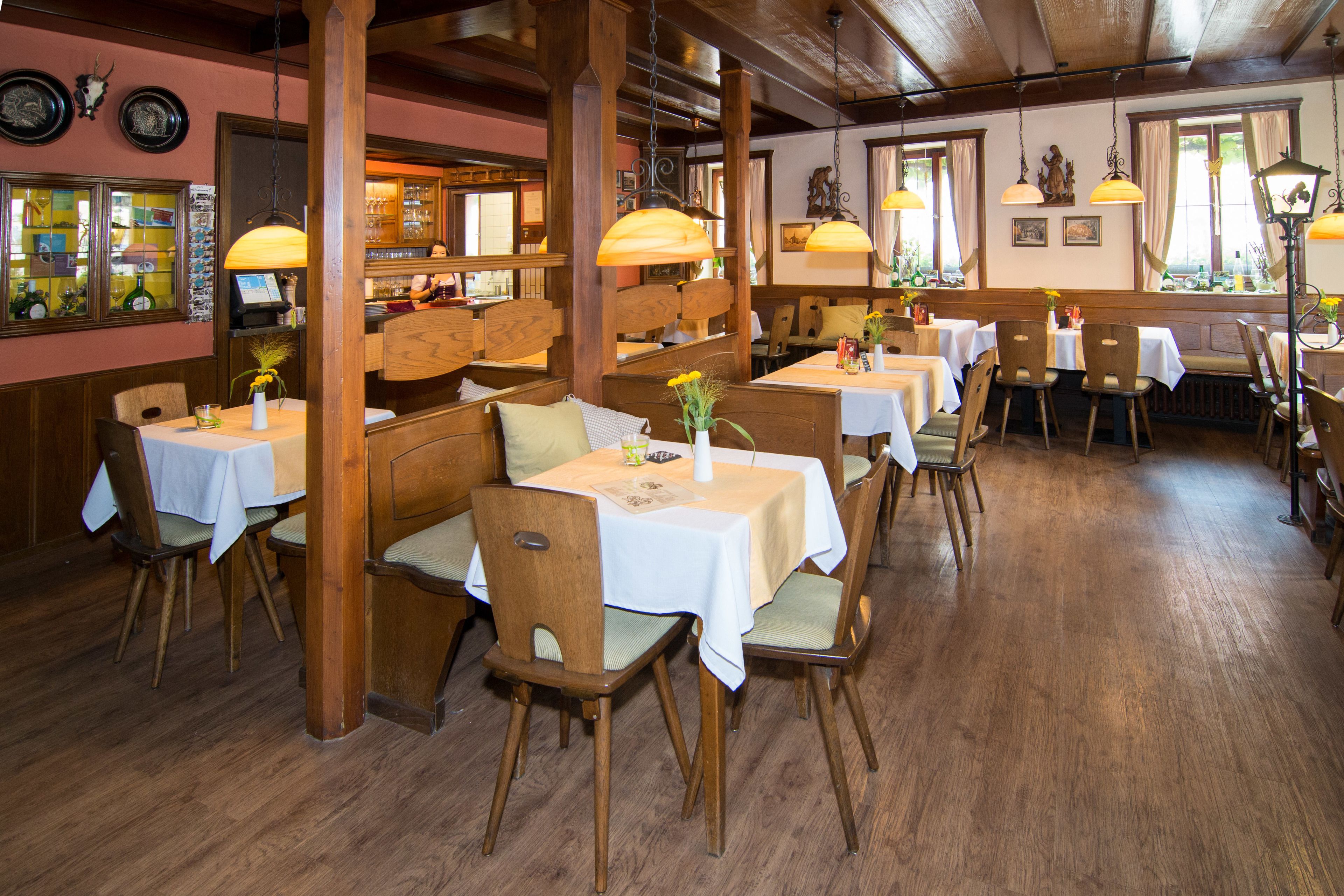 Ein Restaurant mit Holzkasteln und Tischen, das ein warmes Ambiente mit Holzbalken und Pendelleuchten bietet.