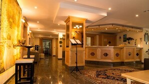 Un amplio vestíbulo de hotel con piso de mármol, una isla central con un piano y una alfombra grande.