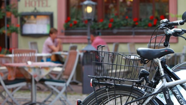 Una bicicleta con una canasta en la parte trasera, estacionada frente a un edificio con un letrero que dice 'HOTEL'.