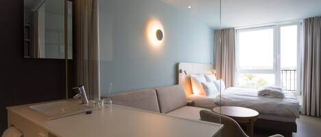 A modern hotel room with a large bed, a sofa, a desk, and a bathroom.
