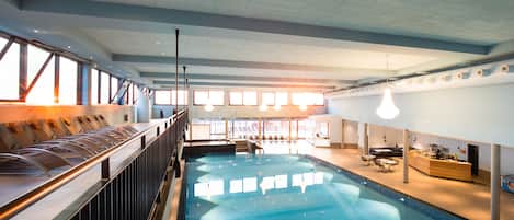 An indoor swimming pool with a bar area, seating, and a reception desk.