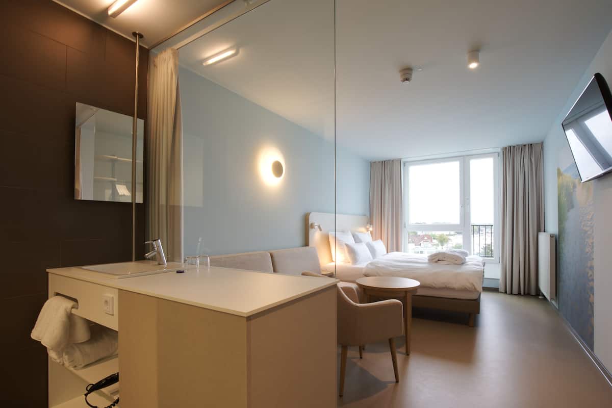 Une chambre d’hôtel moderne avec un grand lit, une table de chevet, une chaise, un bureau et un grand miroir.