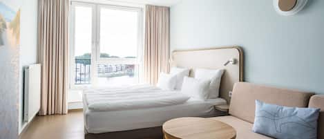 Habitación de hotel con cama, sofá, una mesita y vistas a la ciudad a través de amplios ventanales.