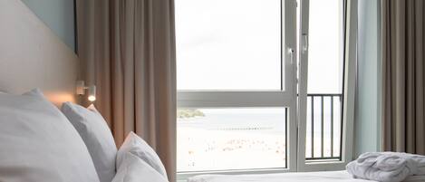 Habitación de hotel con dos camas, una ventana con cortinas y vista a la playa.