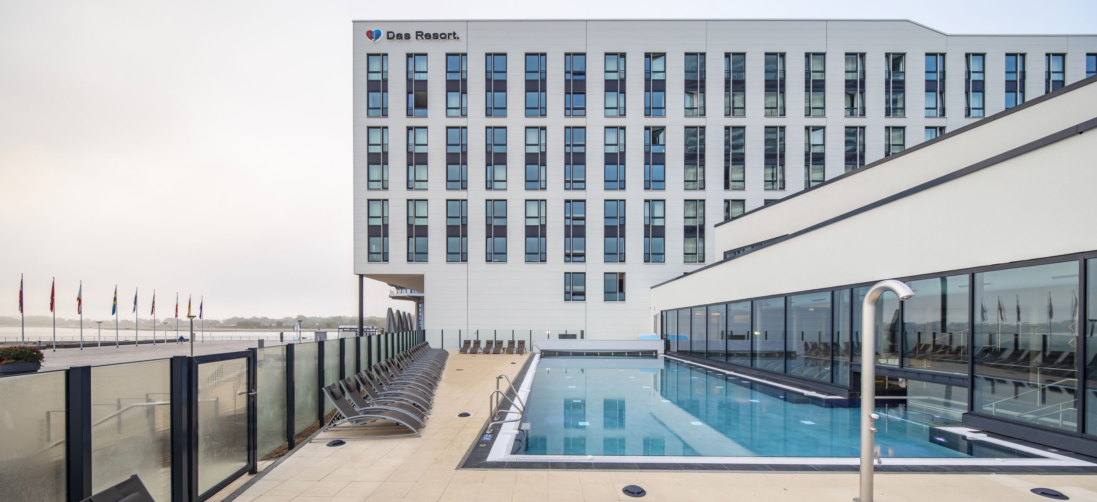 Un edificio moderno con piscina, pabellones de banderas y cielo despejado.