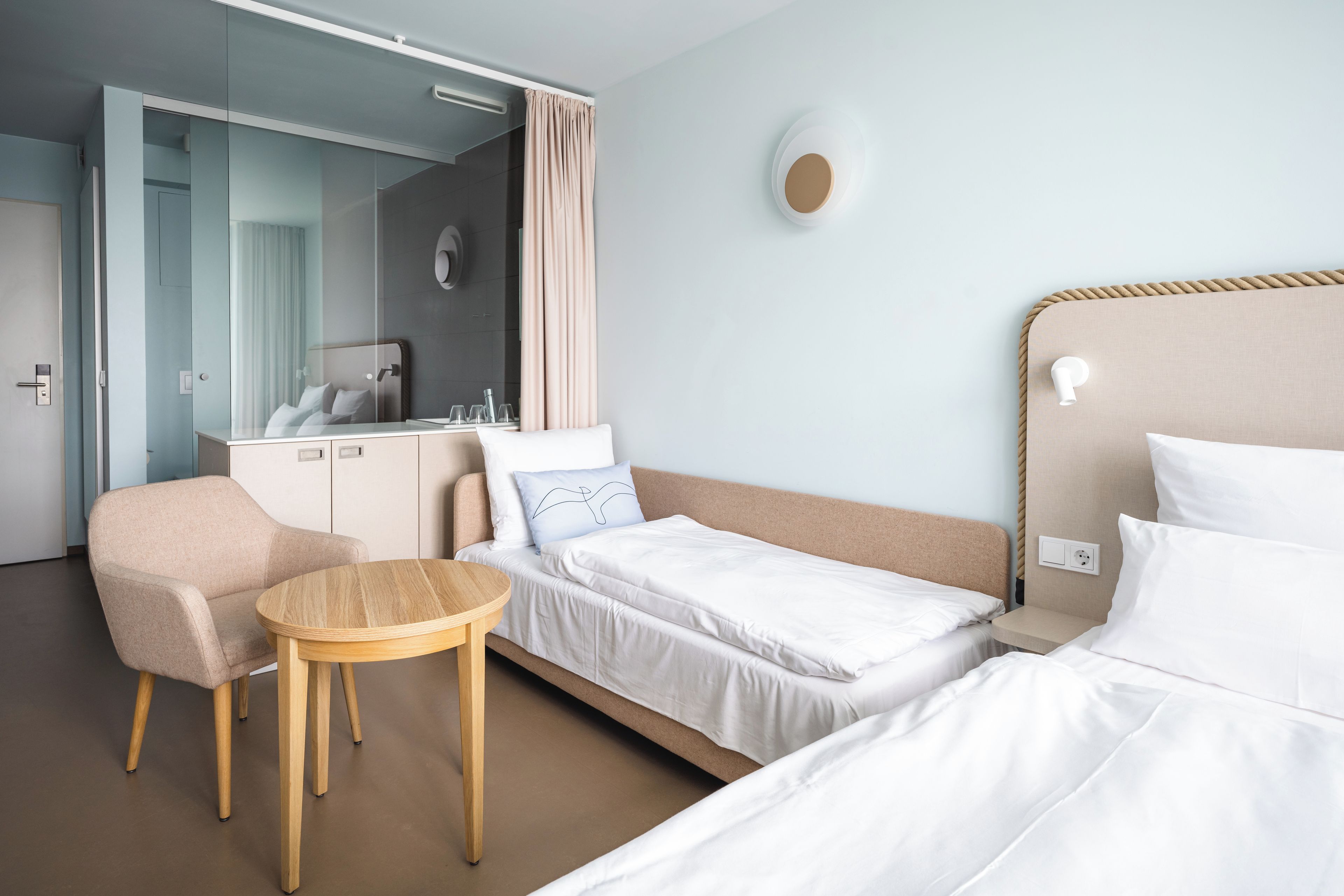 Ein Hotelzimmer mit Bett, Sessel, Nachttisch, Kleiderschrank und Spiegel.