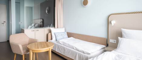 A hotel room with a bed, a chair, a small table, a wardrobe, and a mirror.