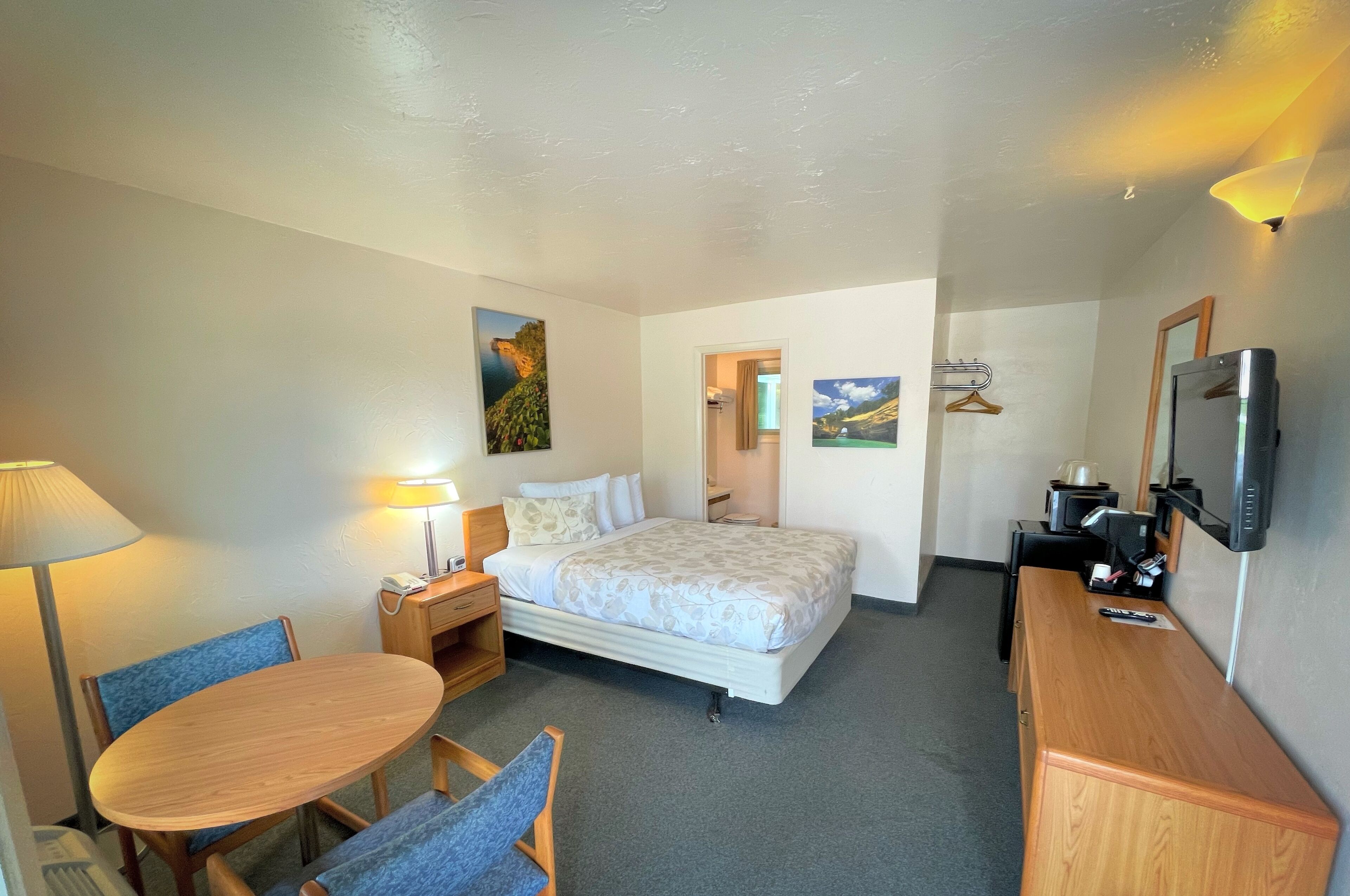 A hotel room with a bed, a desk, a chair, a lamp, and a TV.