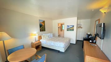 A hotel room with a bed, a desk, a chair, a lamp, and a TV.