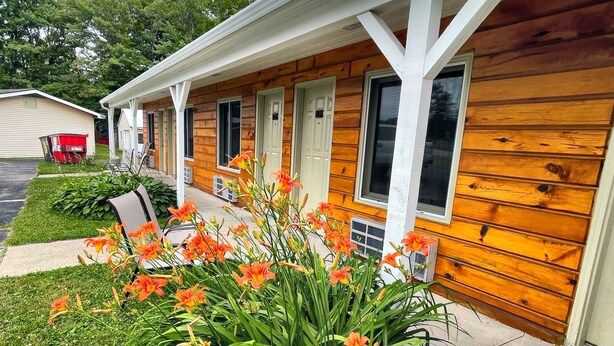 A wooden cabin with a porch, a small garden with orange flowers, and a clear sky. - Alger Falls Motel (Munising)