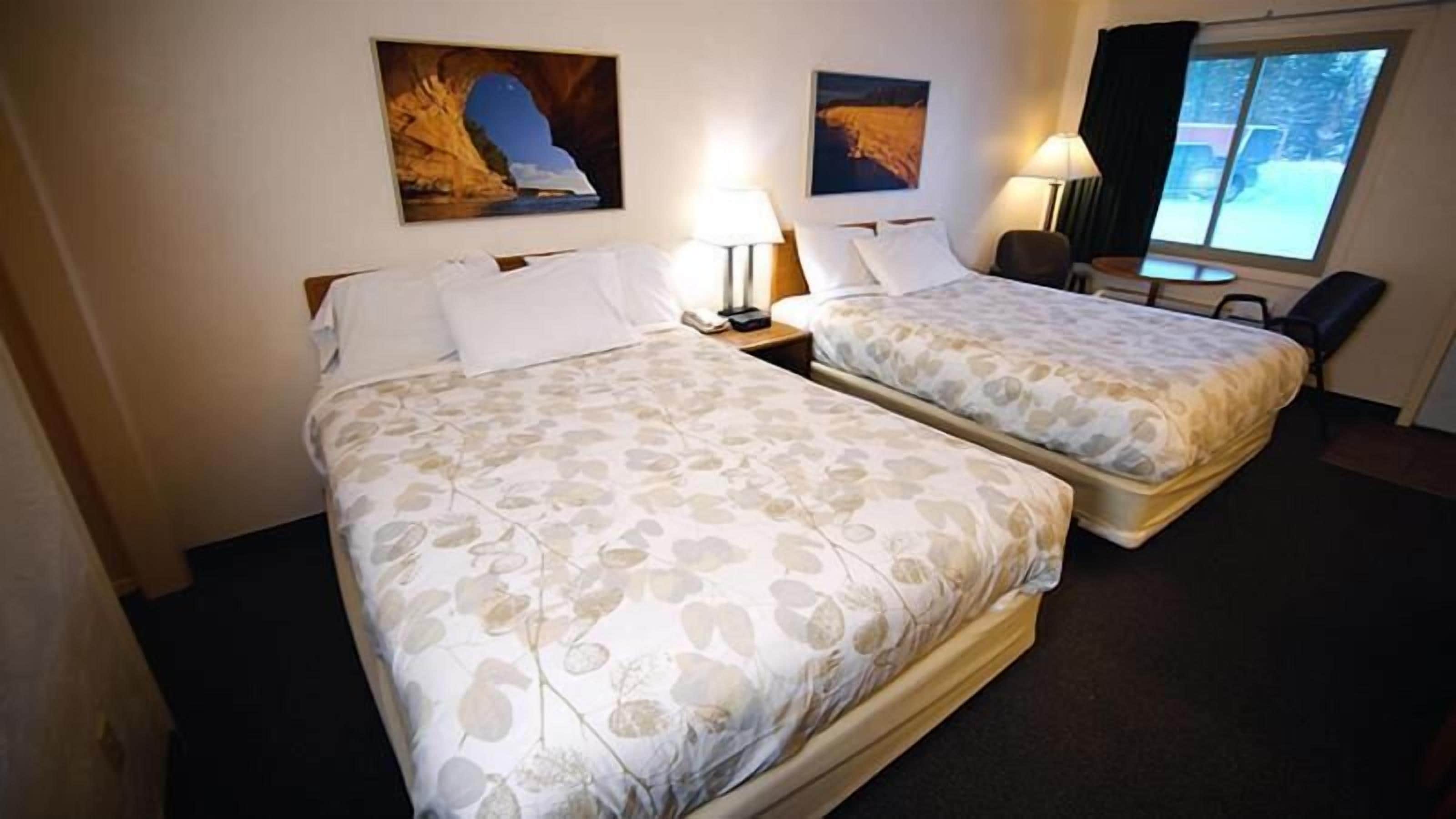 Une chambre d’hôtel avec deux lits, une fenêtre et des œuvres d’art accrochées aux murs.