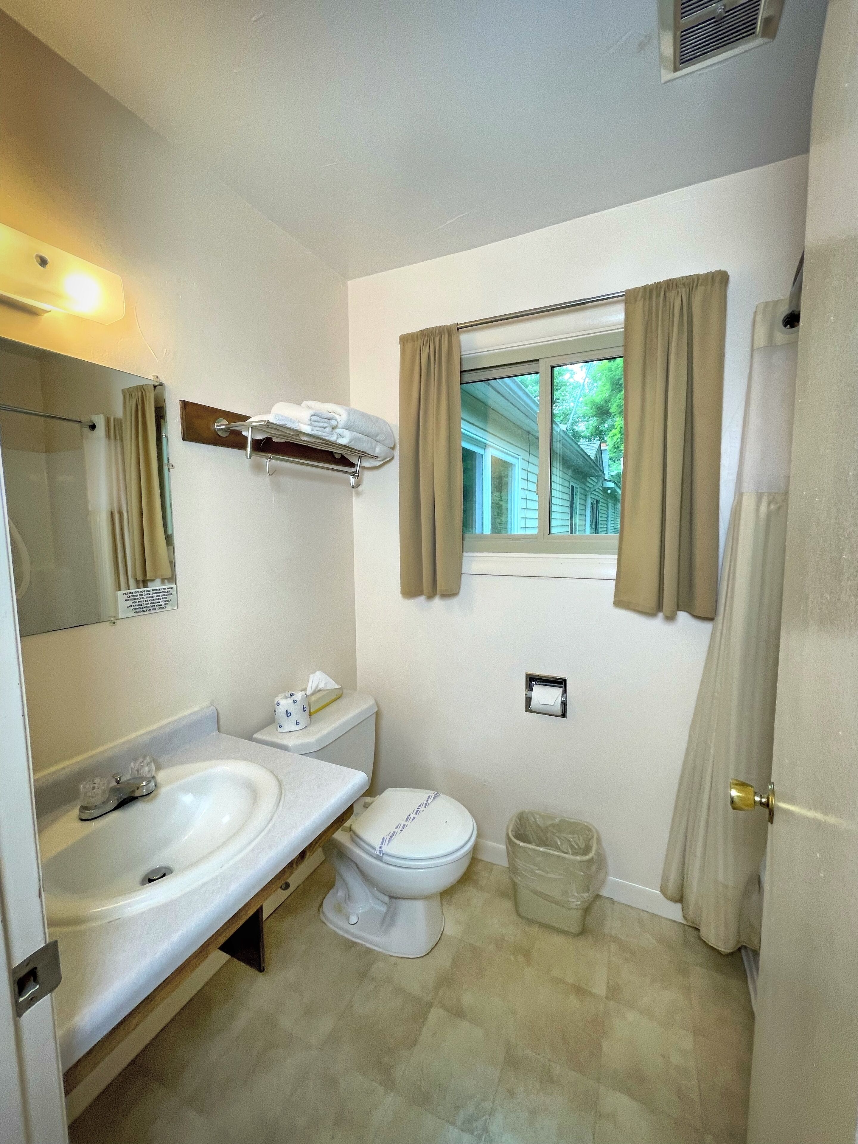 A bathroom with a sink, toilet, and a window with curtains.