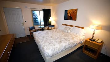 Een hotelkamer met een bed, een bureau, een stoel, een klein tafeltje, een lamp en een schilderij aan de muur.