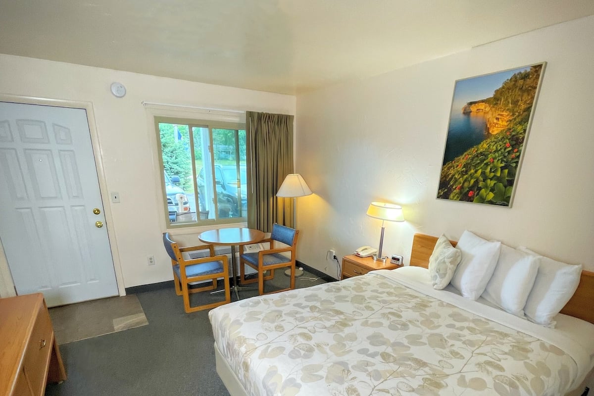 A hotel room with a bed, a desk, a chair, a table, and a painting on the wall.
