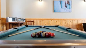 A pool table with balls, a wooden wall, two wall-mounted lights, and a painting of a snowy landscape. - Alger Falls Motel (Munising)