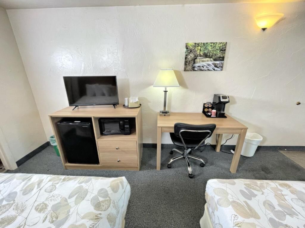A hotel room with a bed, a desk with a computer, a TV, a lamp, and a coffee machine.