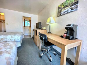 A hotel room with a bed, a desk with a chair, a TV, a coffee maker, and a painting on the wall. - Alger Falls Motel (Munising)