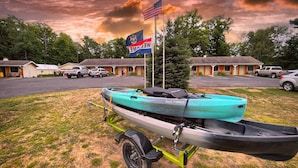 A turquoise canoe on a trailer in front of a motel with a flag, parked cars, and a cloudy sky. - Alger Falls Motel (Munising)