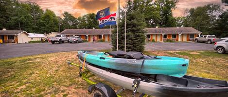 A turquoise canoe on a trailer in front of a motel with a flag, parked cars, and a cloudy sky.