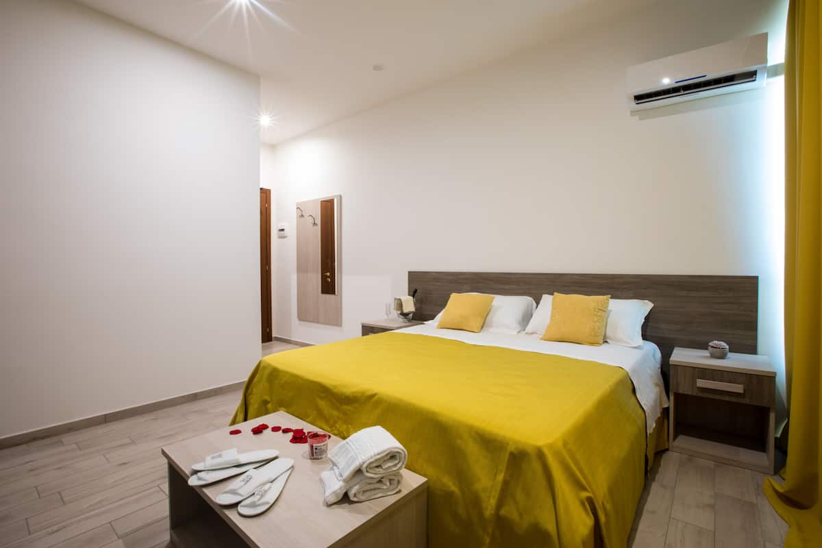 Una habitación de hotel con cama, mesitas de noche, aire acondicionado y suelo de madera.