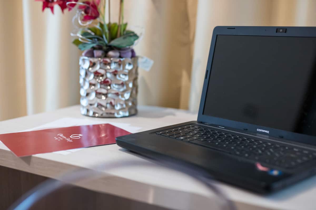 Una laptop sobre una mesa con un jarrón decorativo y un folleto rojo.