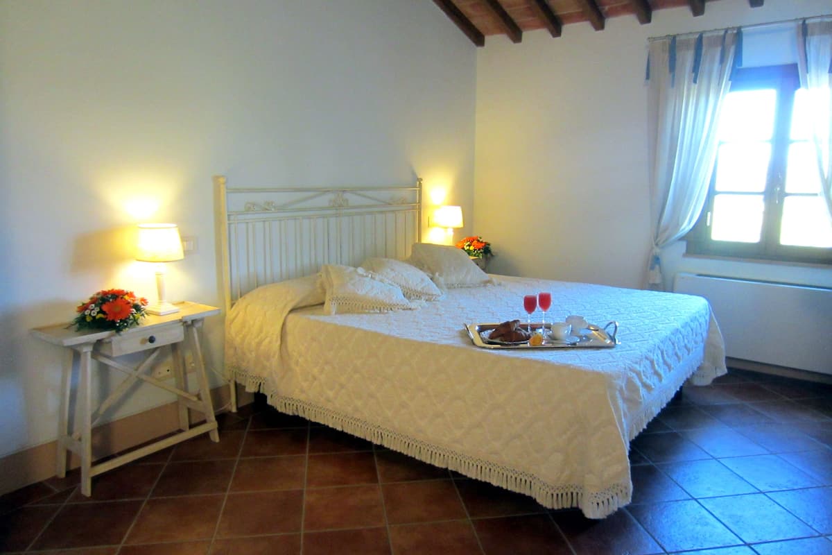 A neatly made bed with a tray of breakfast items, two bedside lamps, and a window with curtains.
