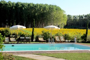 A swimming pool with lounge chairs and umbrellas, surrounded by a flower garden and trees. - Le Colombaie Country Resort (Ponsacco)