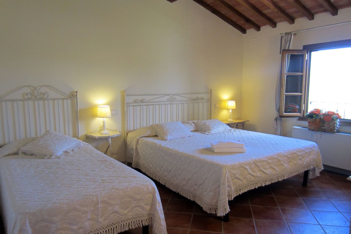 A room with two beds, each with a white bedspread and matching pillows, flanked by bedside tables with lamps.