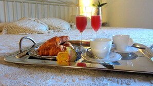 A breakfast tray with croissants, a fruit, two glasses of red beverage, and white cups on a bed with a white headboard and pillows. - Le Colombaie Country Resort (Ponsacco)