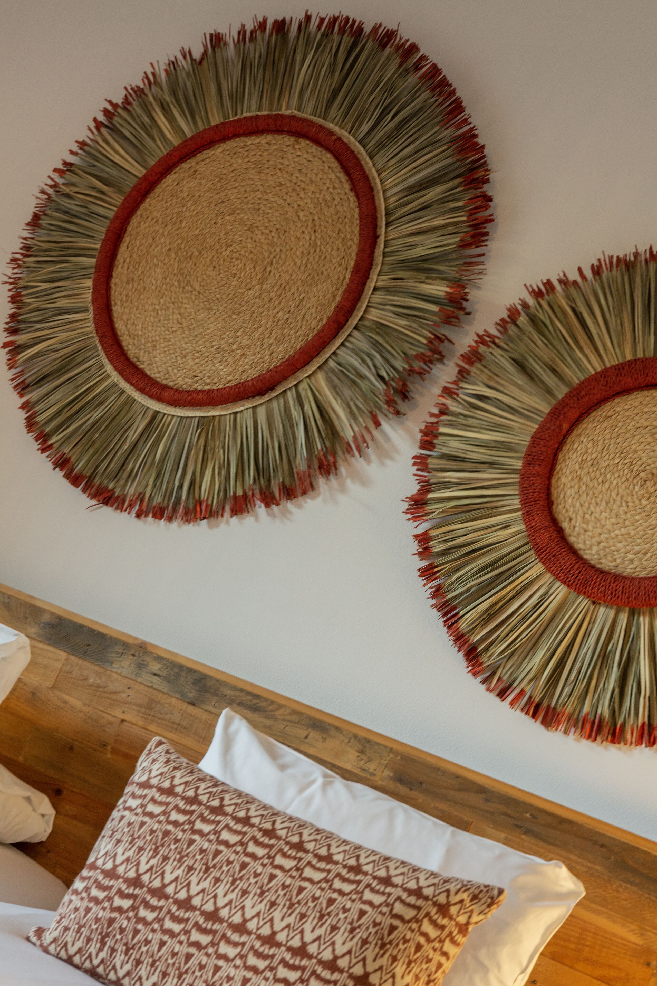 A room with a wooden headboard, a bed with white and patterned pillows, and two wall-mounted circular wall hangings with fringe details.