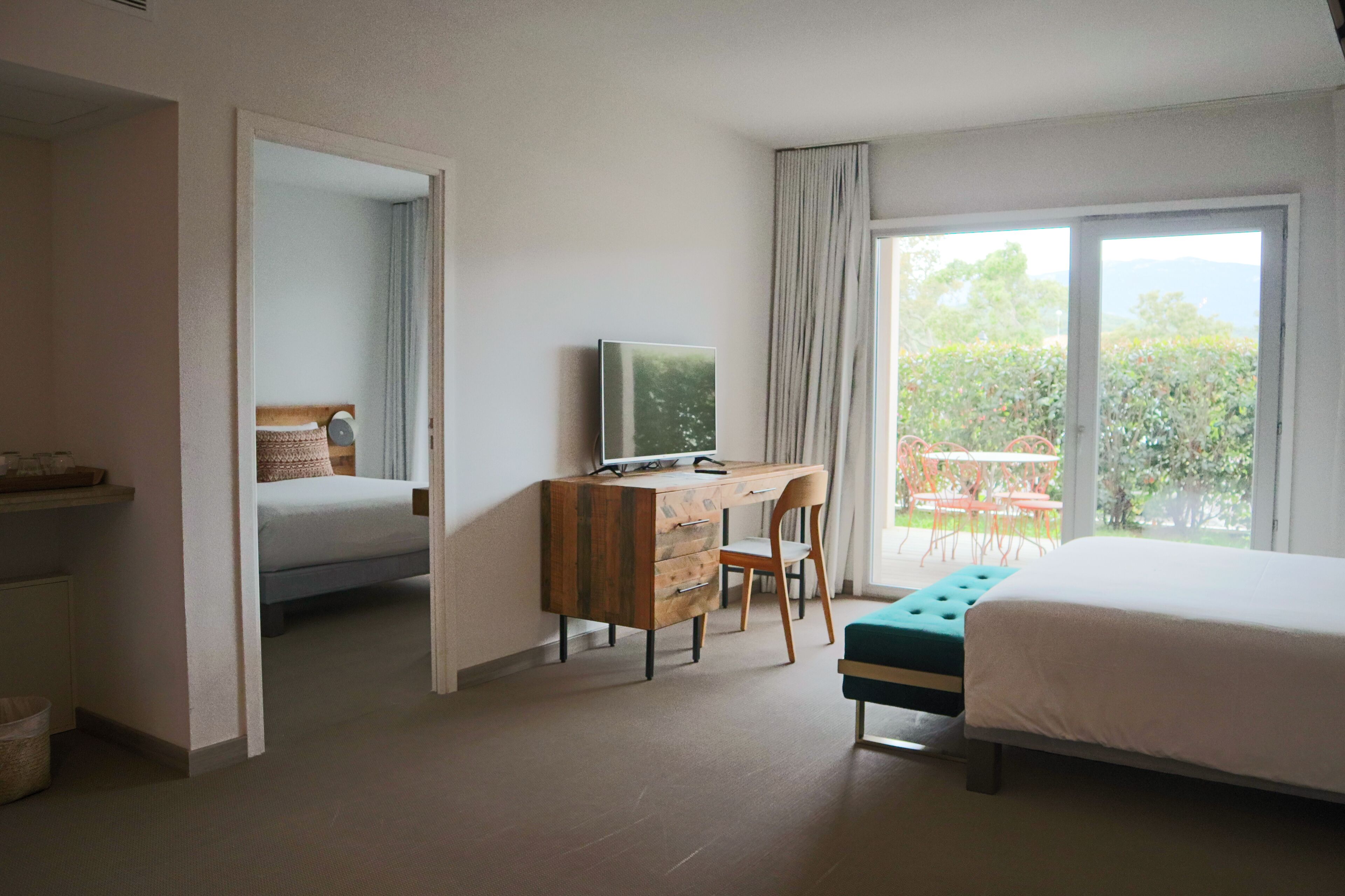 Habitación de hotel con cama, escritorio con computadora, silla, ventana con cortinas y vista a zonas verdes.