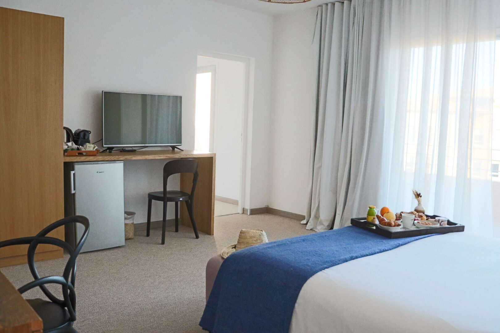 Een hotelkamer met een bed, een bureau met een televisie, een stoel en een ontbijtbakje op de vensterbank.