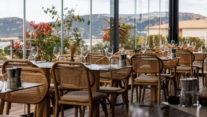 Restaurante com mesas preparadas para refeições, cadeiras de vime e vista para as montanhas.