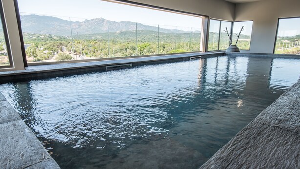 Piscina interior moderna com amplas janelas que oferecem vista para uma paisagem montanhosa.