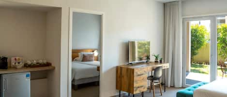 A hotel room with a bed, a desk with a computer, a small fridge, and a view of the outdoors.