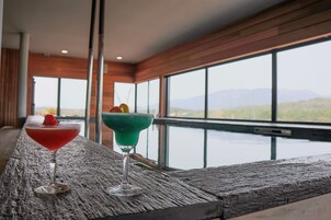 Dos cócteles sobre una barra de madera con ventanas amplias que ofrecen vistas a montañas.