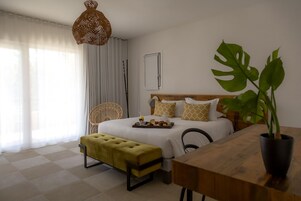 Una habitación de hotel moderna con cama, mesita de noche, banco y planta en maceta.