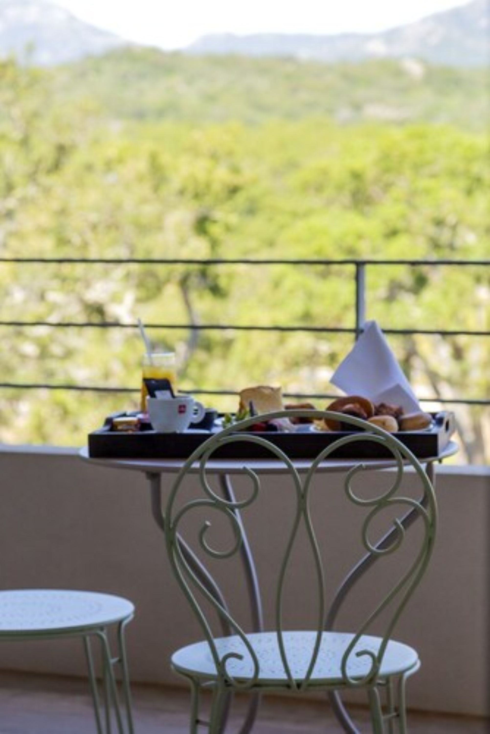 A balcony with a table set for breakfast, overlooking a mountainous landscape.