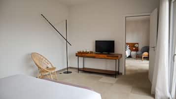 Une chambre d’hôtel avec un lit, une chaise en osier, un bureau avec une télévision et une vue sur une autre chambre.