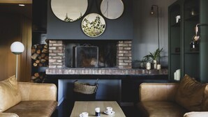 Um interior acolhedor com sofás de couro, uma mesa de madeira com chávenas, uma lareira de tijolo e pratos decorativos na parede.
