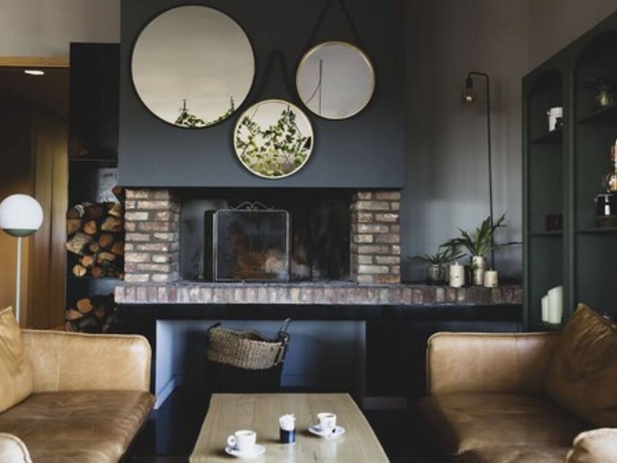 Un interior acollidor amb sofàs de pell, una taula de fusta amb tasses, una llar de pedra i plats decoratius a la paret.