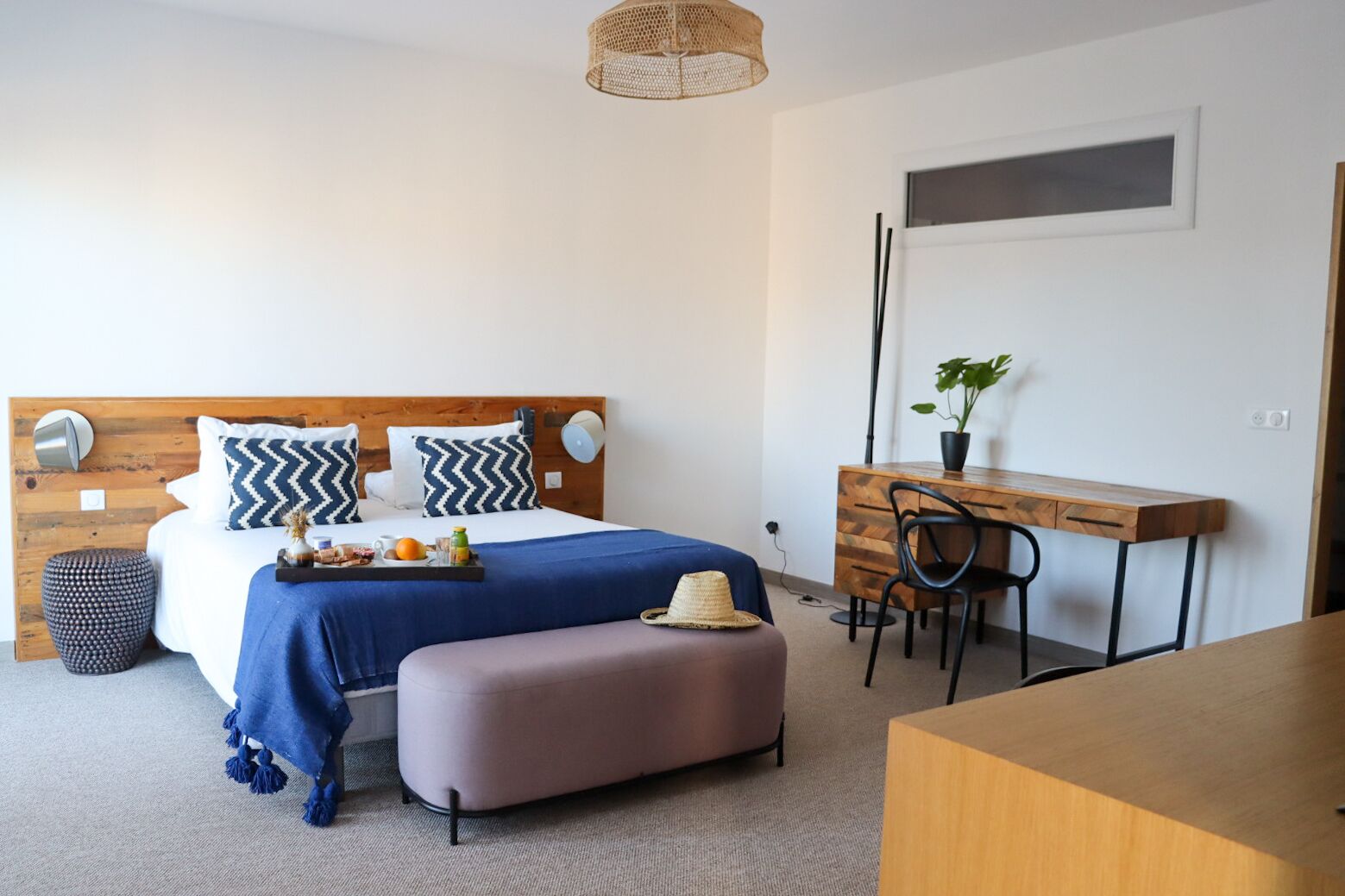 A bedroom with a bed, bedside table, desk, chair, and a small potted plant.