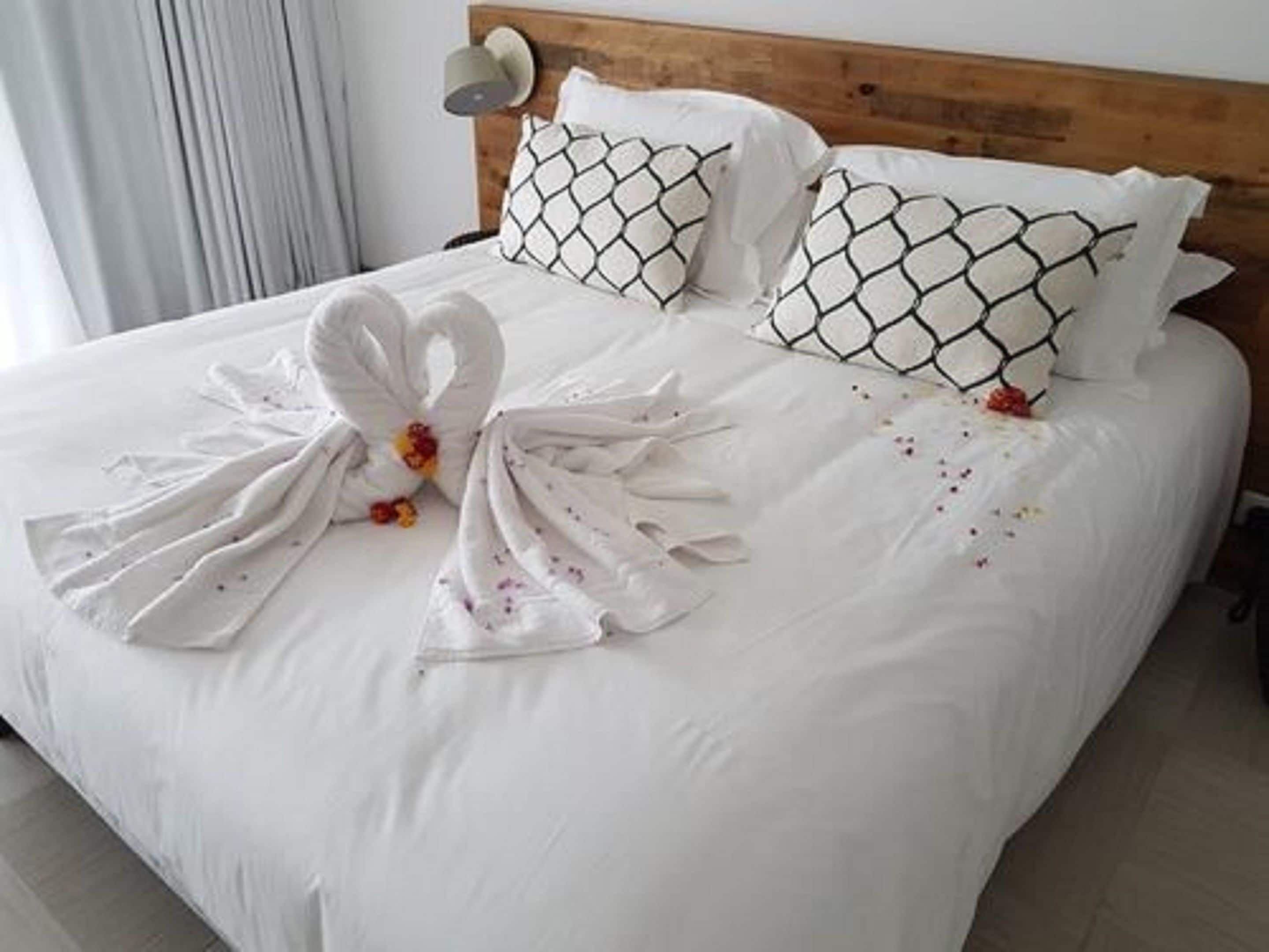Una cama bien hecha con sábanas blancas y dos toallas dispuestas en forma de cisne.