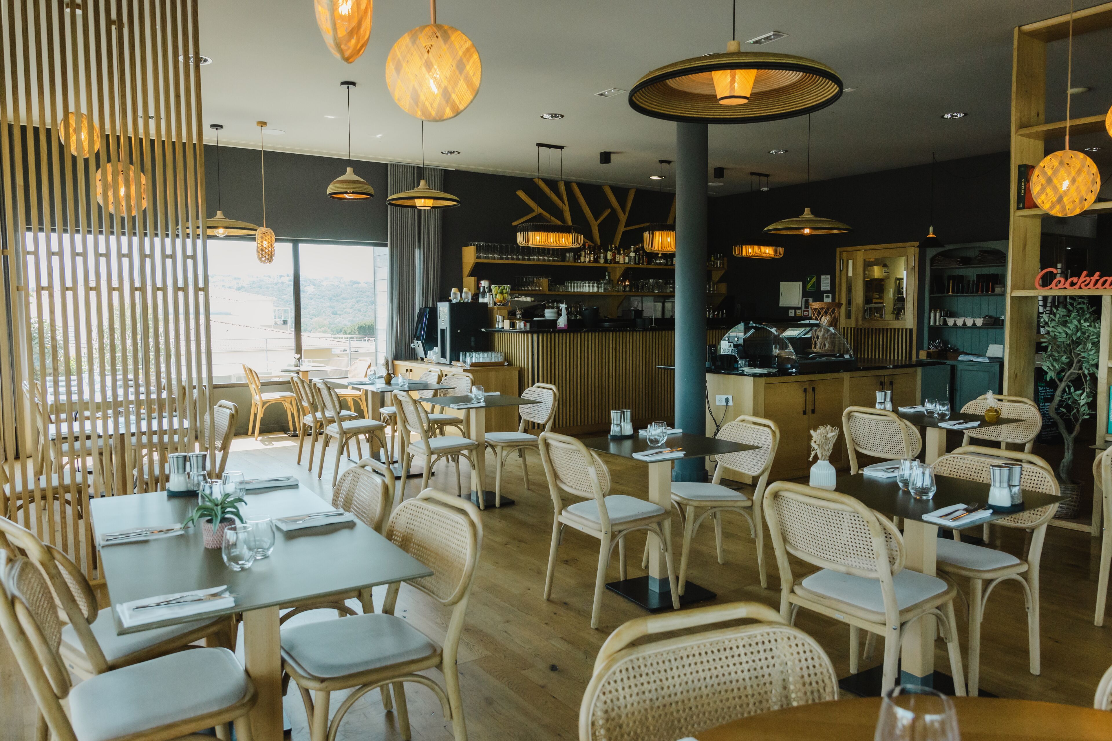 Restaurante com mobiliário de madeira, luminárias pendentes e um espaço de bar.
