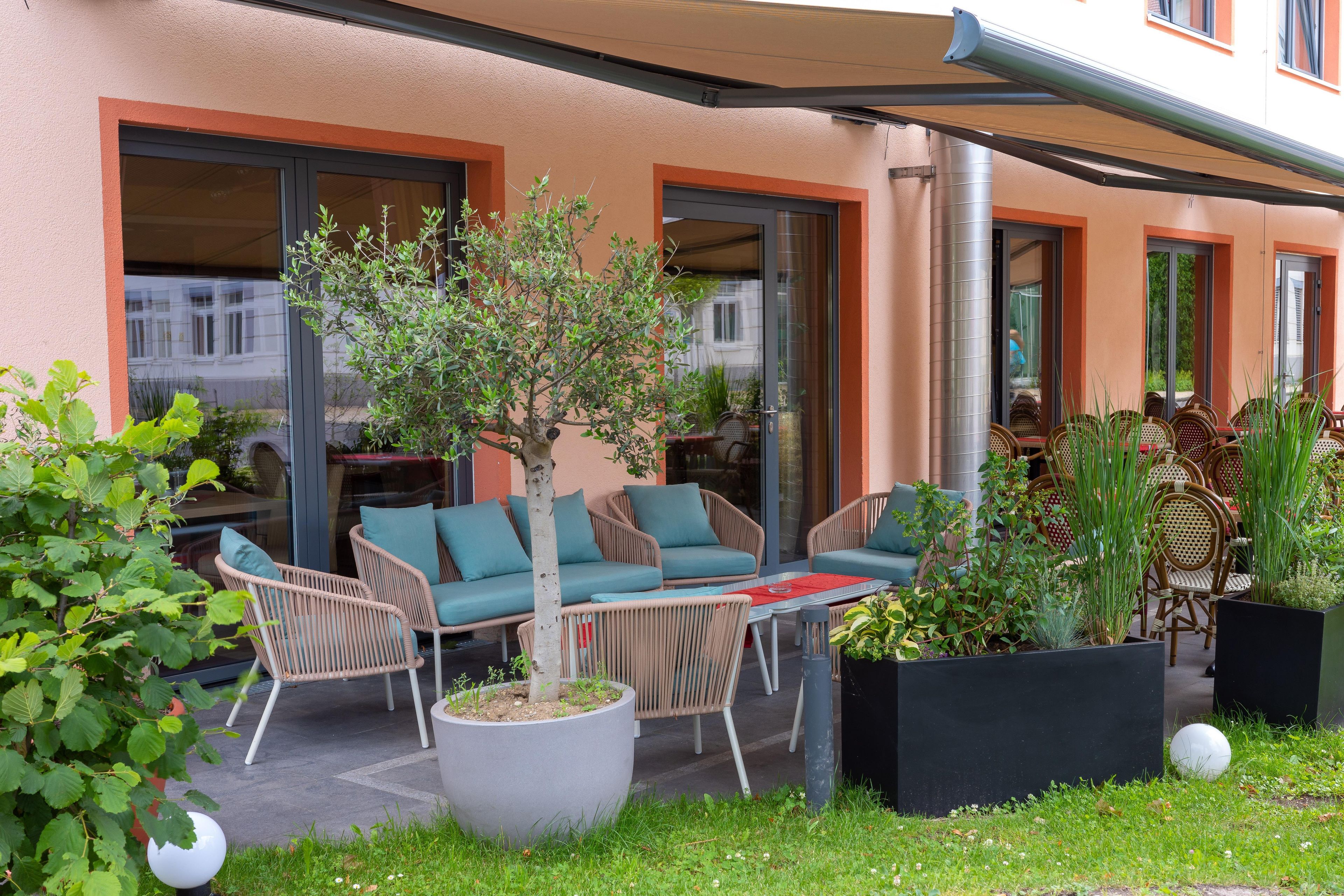 Un área de estar al aire libre con muebles de mimbre y un macetero central con un árbol.