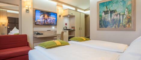 Una habitación de hotel con dos camas, un sofá rojo, un televisor, un cuadro y un minibar.