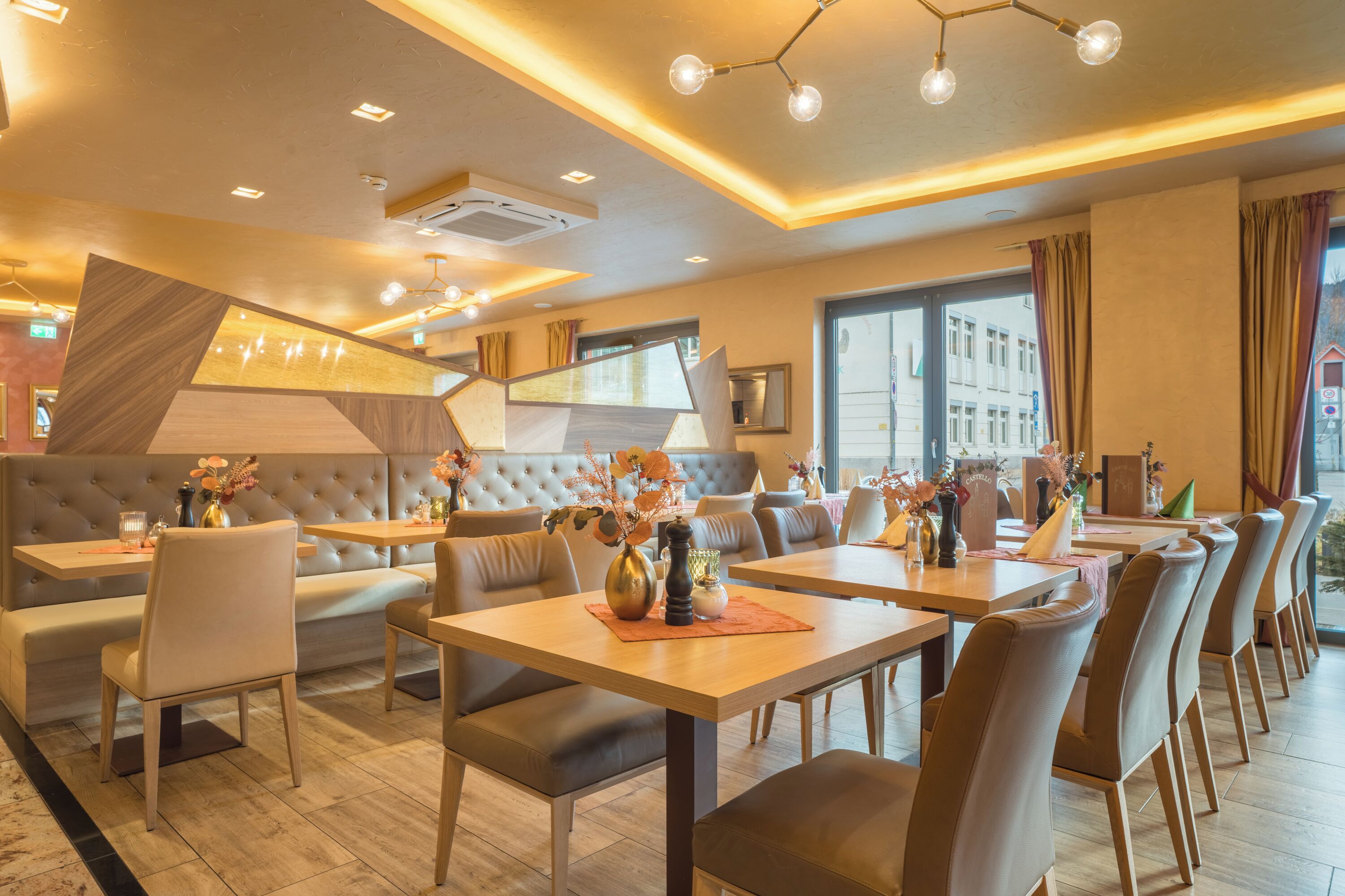A modern restaurant with a mix of booth and table seating, featuring a central decorative wall and large windows.