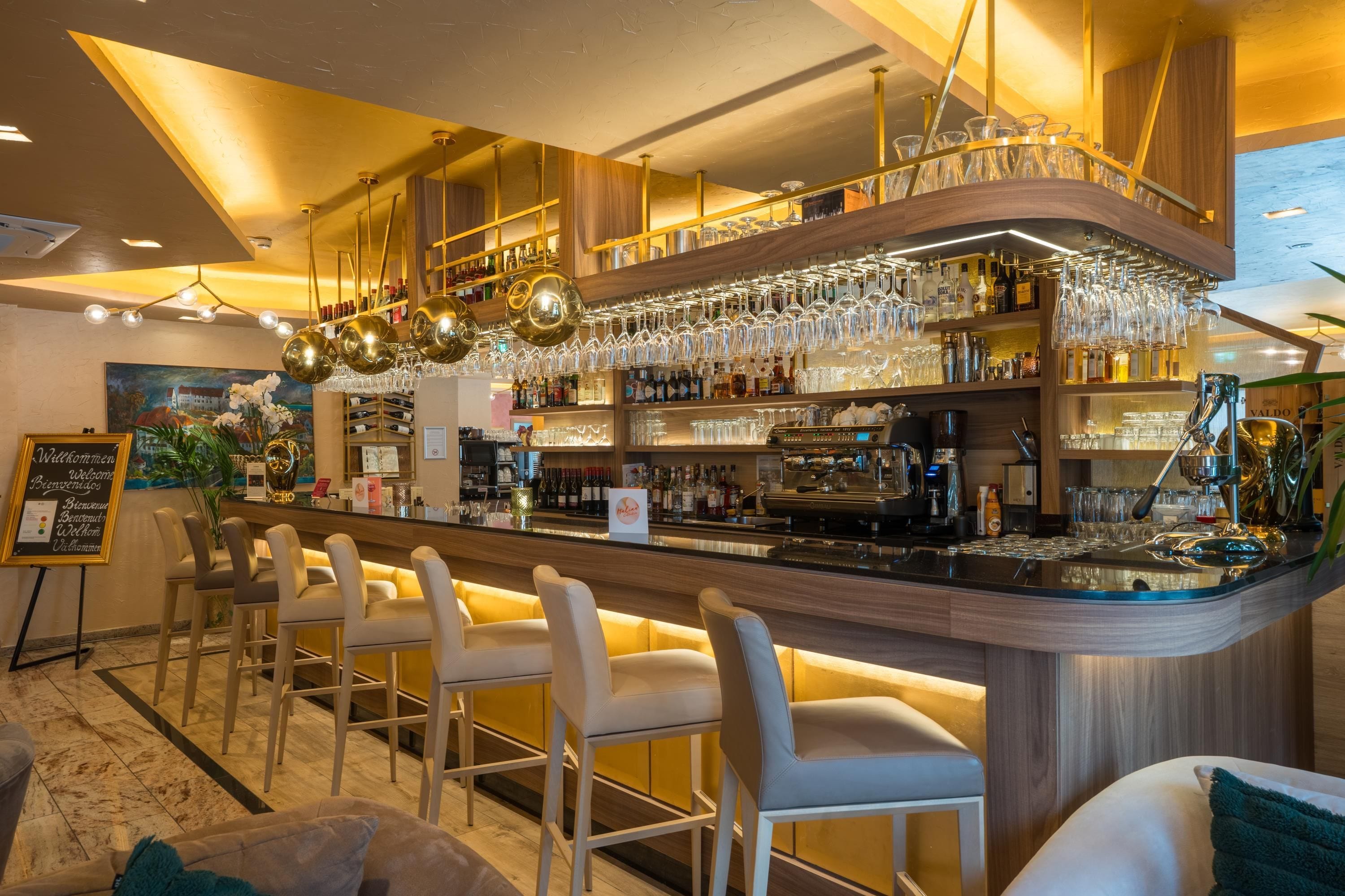 A bar area with a counter, bar stools, and a variety of bottles and glasses.