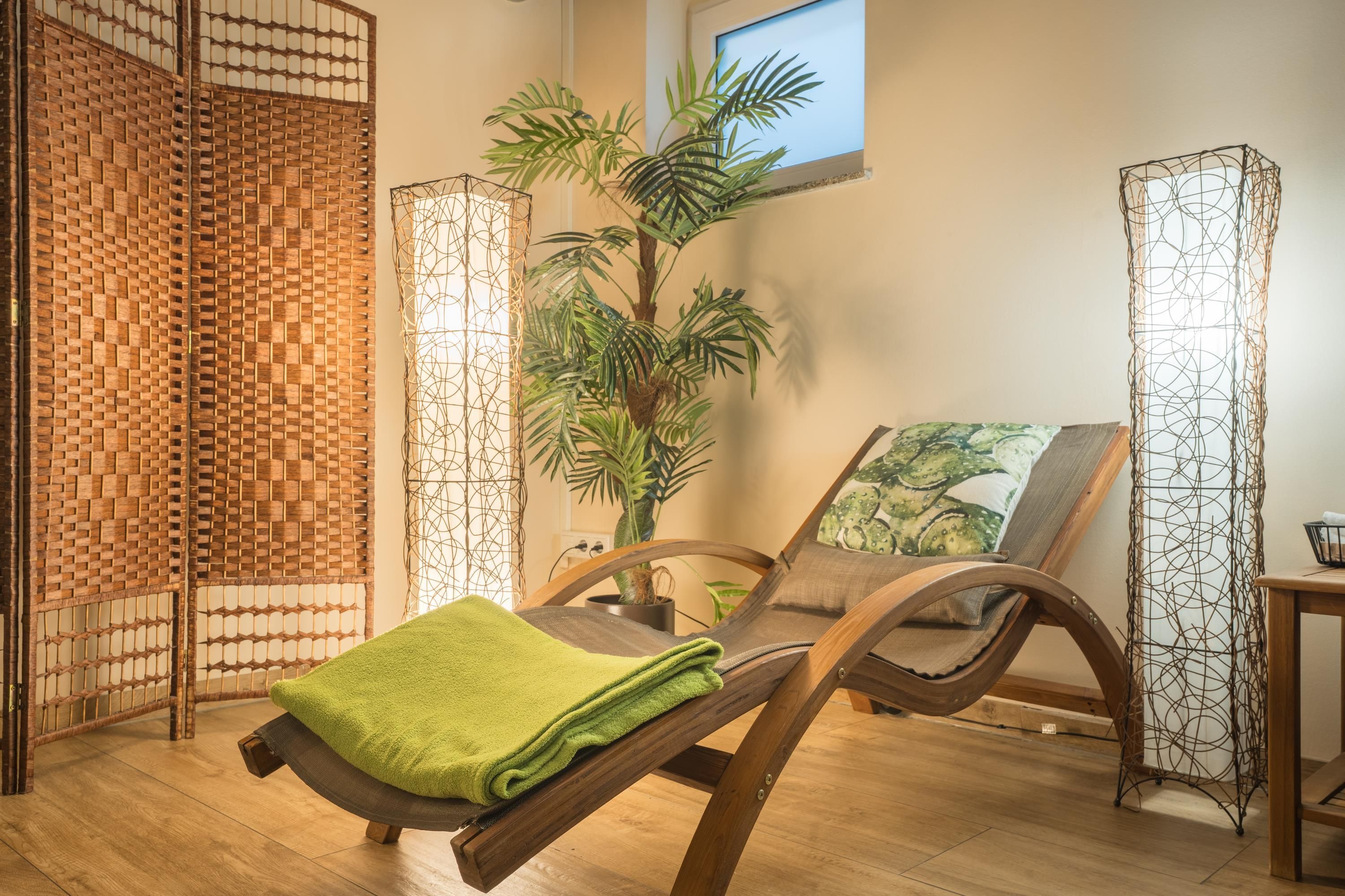 Un cuarto de spa con una mesa de masaje de madera, una toalla verde, una planta grande en maceta y una ventana con vistas.