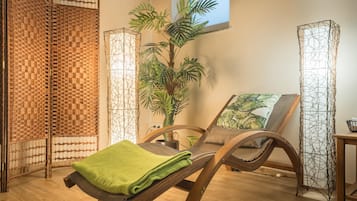 Un cuarto de spa con una mesa de masaje de madera, una toalla verde, una planta grande en maceta y una ventana con vistas.